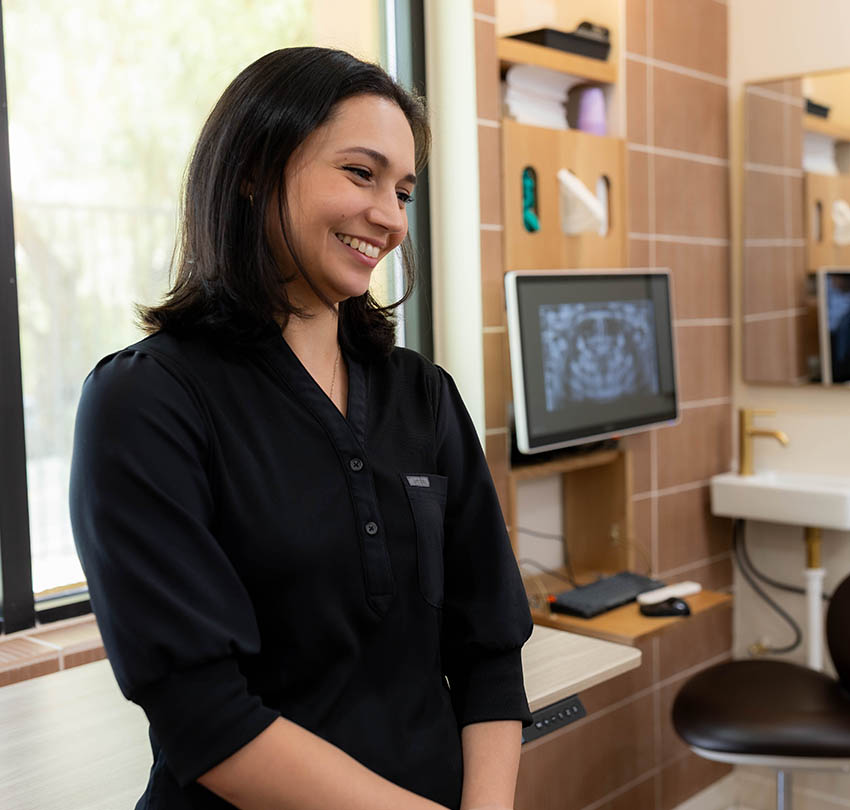 Smiling dental team member beside a treatment chair and digital imaging screen